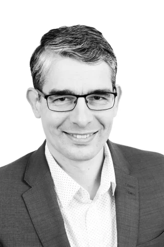 Black and white image of a man wearing glasses. the image includes the man's head and shoulders