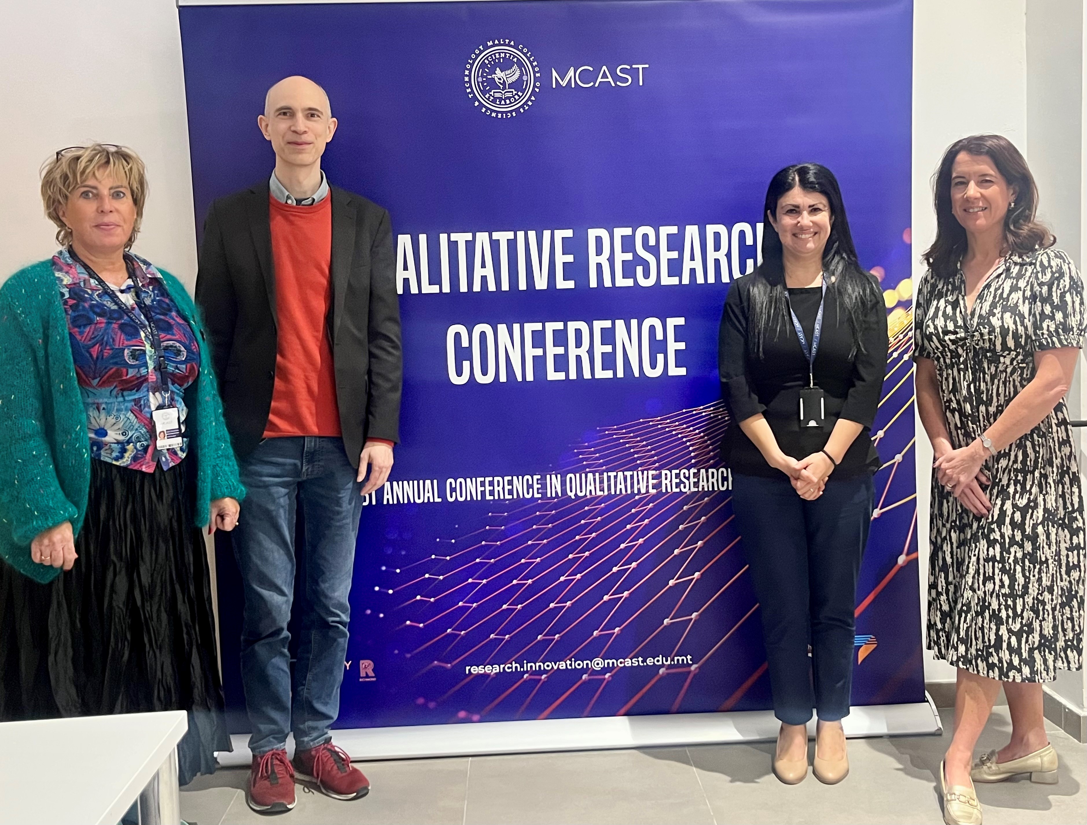 Four people standing in front of a display stand advertising a conference