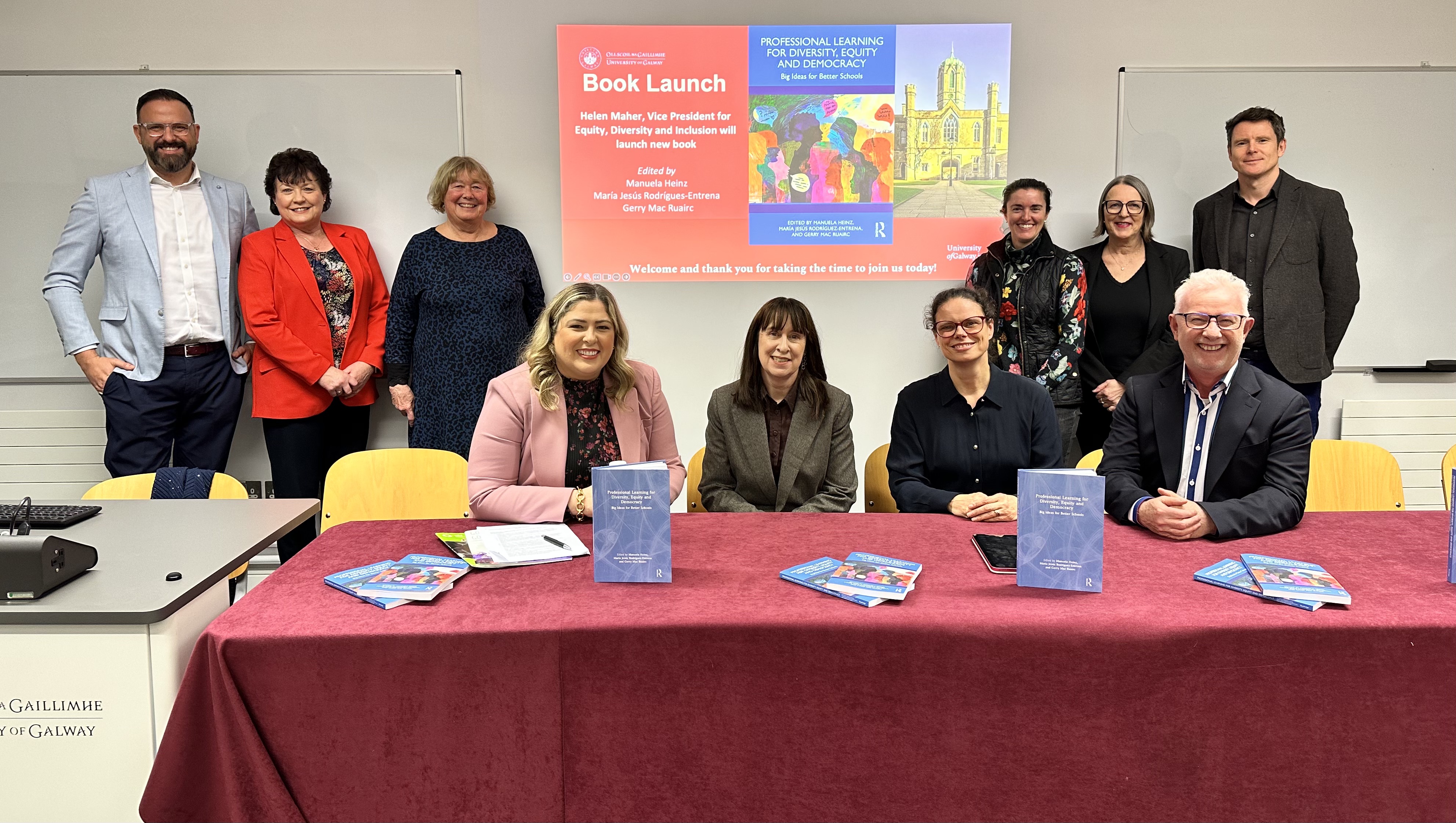 Group photo of key people sitting at front of room with image of book launch details behind them