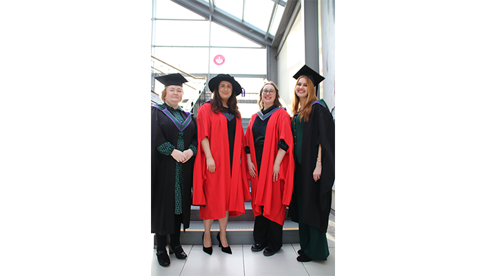 Four people wearing conferring robes stood in front of a glass window